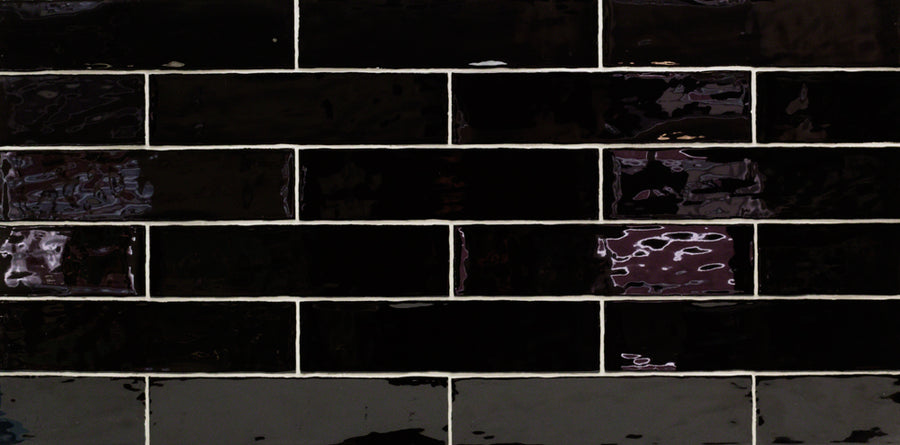 The Masia 3" x 12" Subway Tile in Nero features a glossy black finish in a horizontal brick pattern with light grout lines. Ideal for accent walls or kitchen backsplashes, its surface reflects light for striking highlights and subtle tone shifts.