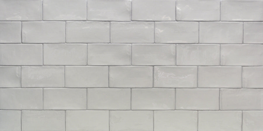 A close-up of a wall with glossy Masia 3" x 6" Subway Tile in Gris Claro, arranged in a horizontal brick pattern. Subtle variations in shade and texture make it ideal for a stylish kitchen backsplash.