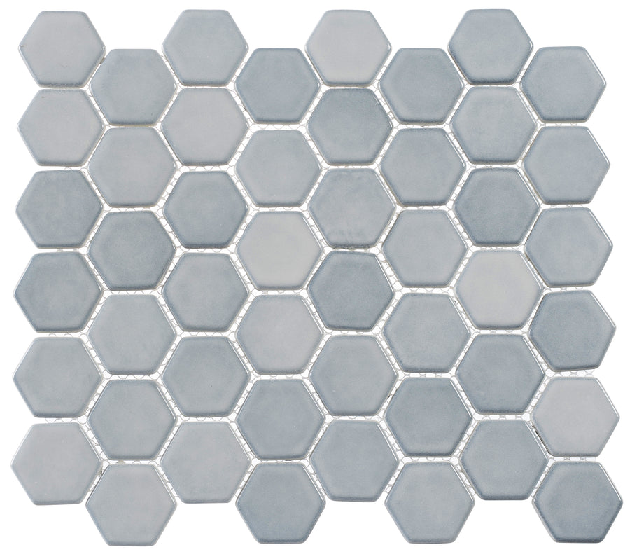 The Greenwich 2" Hexagon Glass Mosaic Tile in Urbanite features small, matte light blue hexagons with thin white grout lines, arranged in a modern honeycomb pattern for a sleek, geometric look.