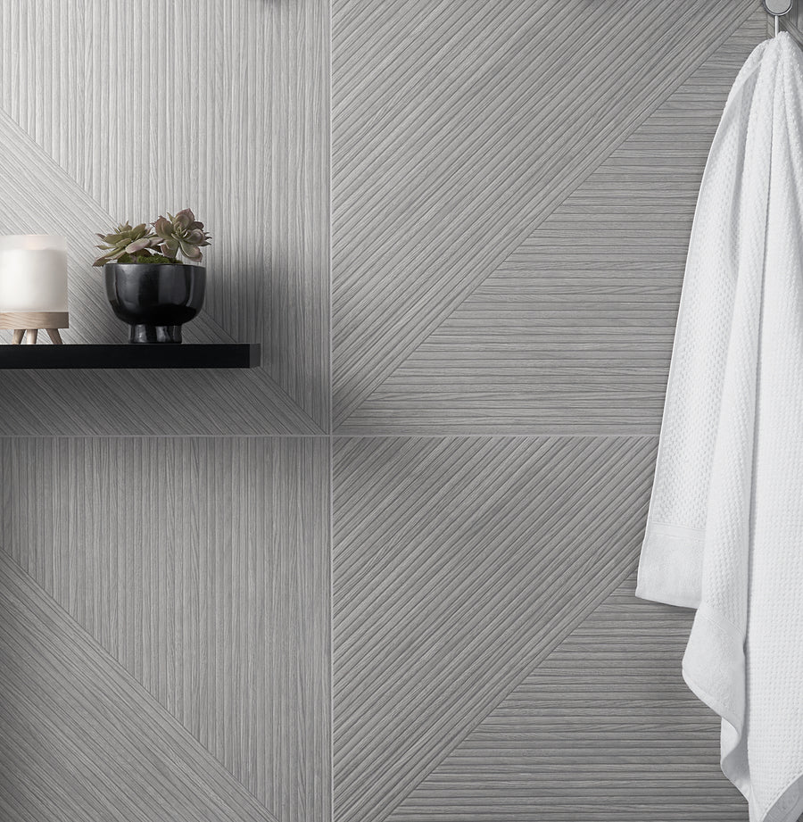 A textured gray tile wall with geometric patterns, a black shelf holding a candle and a small potted plant, and a white robe hanging on the right side.