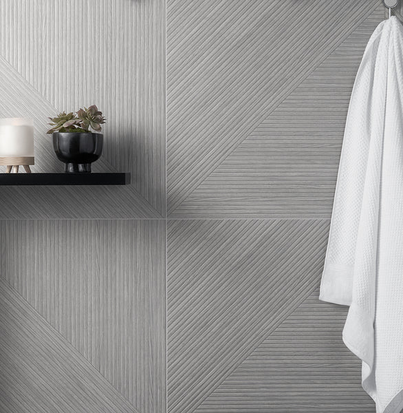 A textured gray tile wall with geometric patterns, a black shelf holding a candle and a small potted plant, and a white robe hanging on the right side.