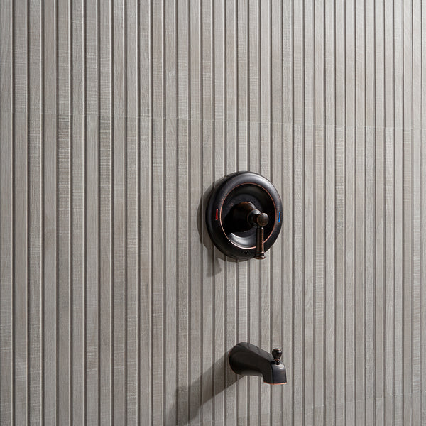 A modern shower faucet with a single-handle control and a tub spout installed on a light gray, vertically textured tile wall.