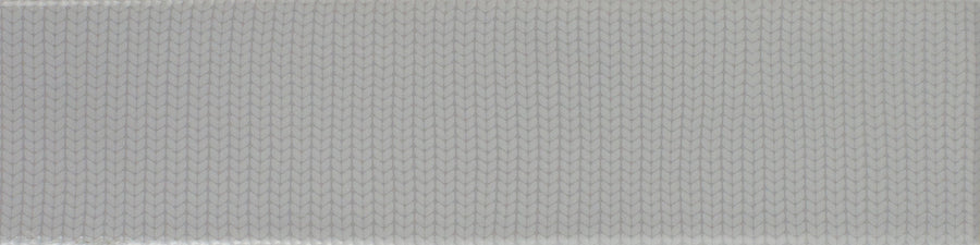 A close-up of the Gradient 3" x 12" Ceramic Tile in Greige Gloss, featuring a textured geometric surface with repeating, overlapping oval shapes reminiscent of fish scales.