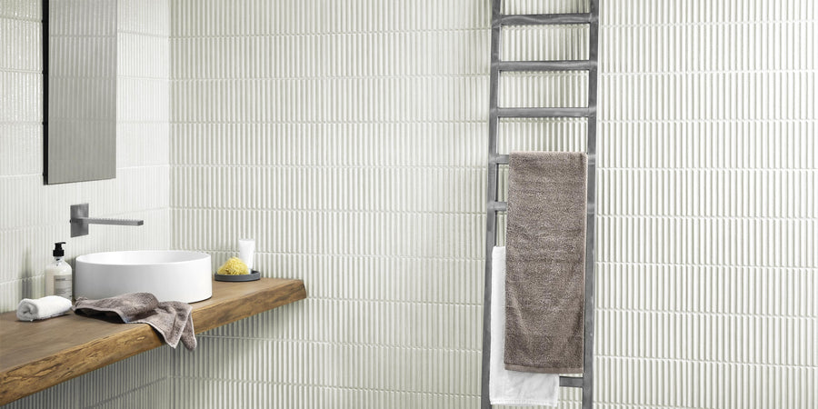 Modern bathroom with Dunes 12x24 Porcelain Tile feature walls, a wooden countertop with a round sink, wall-mounted faucet, soap and towel. A metal towel ladder on the right holds both gray and white towels.