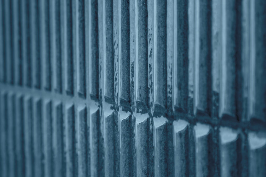 Close-up of a textured wall with vertical, evenly spaced rectangular ridges, illuminated by cool blue light, creating a pattern of shadows and highlights.