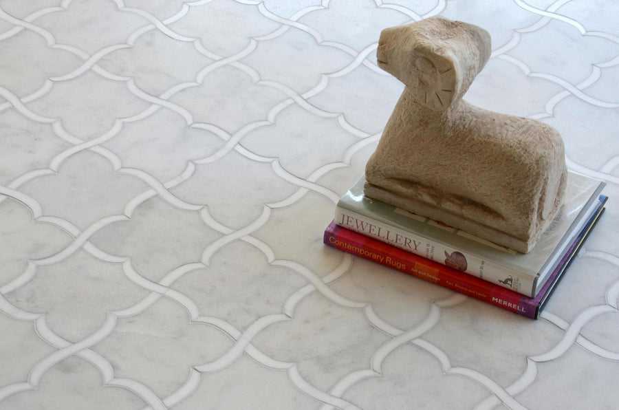 A small stone sculpture of a ram sits atop two stacked books on a white marble floor with an intricate, interlocking geometric tile pattern.