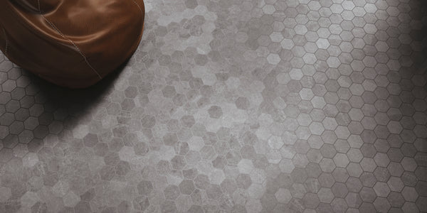 A close-up view of a gray hexagonal tile floor with a smooth, matte finish. In the upper left corner, part of a brown leather object, possibly a bean bag, is visible.
