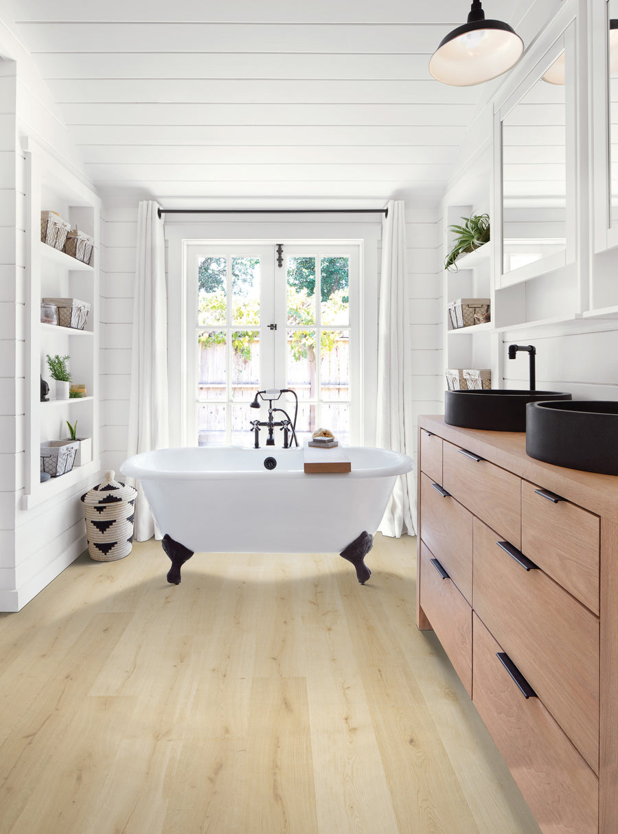 Bright, modern bathroom with a freestanding clawfoot tub near large windows, white walls, open shelves with baskets, light wood floor, and a wooden vanity with black fixtures.