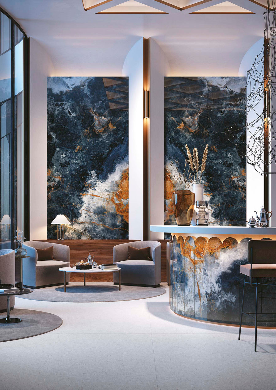A modern lounge area features abstract blue, white, and gold wall art, curved gray armchairs, round tables, and a stylish bar with a matching abstract pattern. Tall windows allow natural light to brighten the sophisticated space.