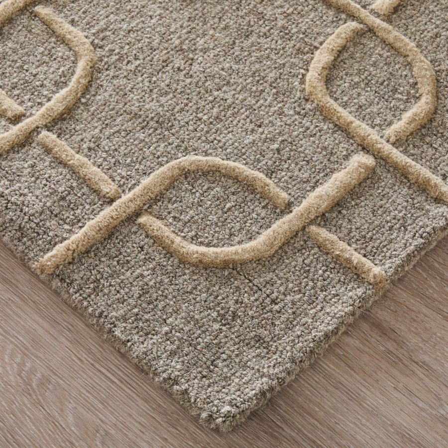 A close-up of a beige textured area rug with a raised, looping geometric pattern, placed on a light wood floor.