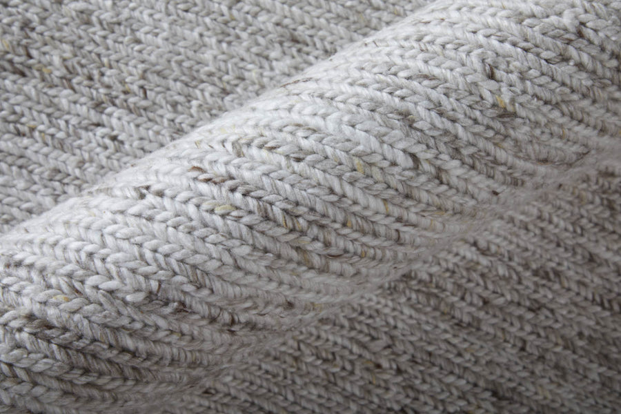 Close-up of a rolled-up light gray knitted fabric with a textured, woven pattern and specks of darker fibers visible throughout.