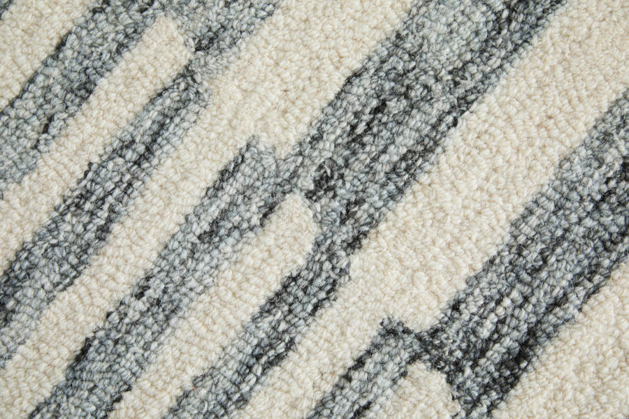 Close-up of a textured carpet with a cream background and irregular vertical gray stripes, creating a modern, abstract pattern.