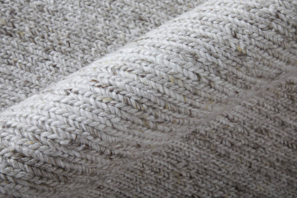 Close-up of a rolled-up light gray knitted fabric with a textured, woven pattern and specks of darker fibers visible throughout.
