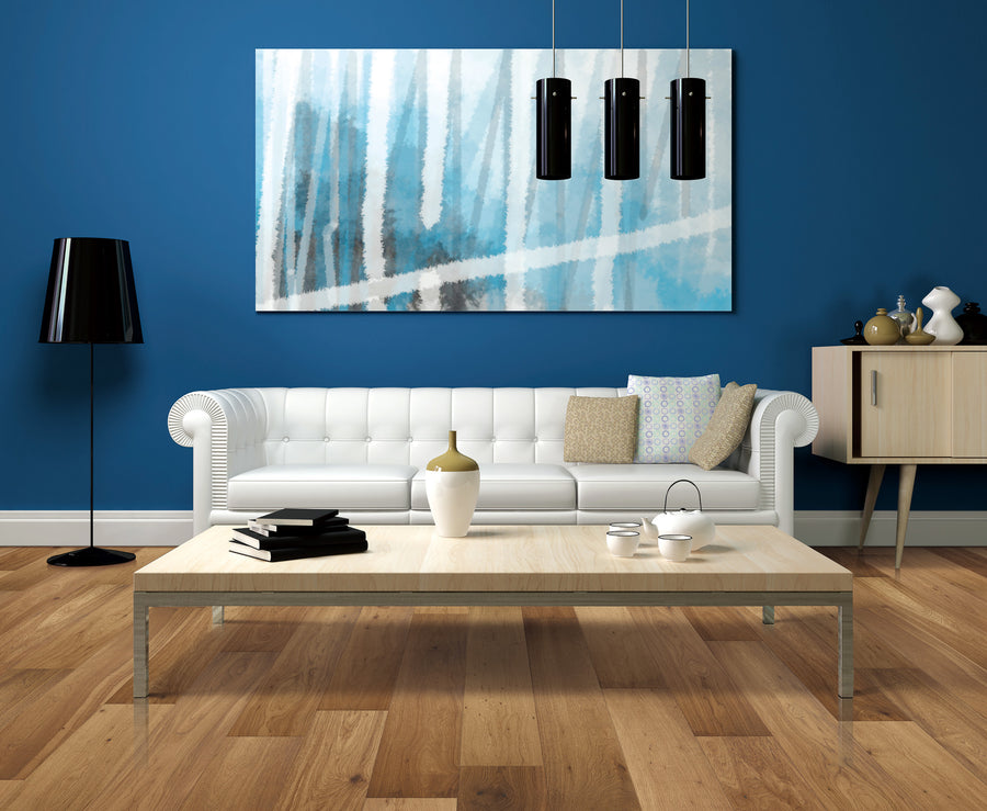 A modern living room with a white sofa, colorful pillows, a wooden coffee table, a black floor lamp, a sideboard, and a large abstract blue and white painting on a blue wall. Three black pendant lights hang above.