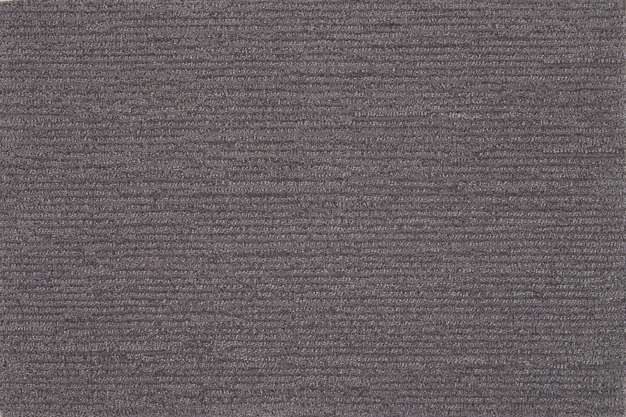 Close-up of Highlands Berber Carpet in Carbon color, showing its textured surface with horizontal ridges. This durable flooring features soft, densely packed fibers and a subtle striped look for a comfortable feel underfoot.