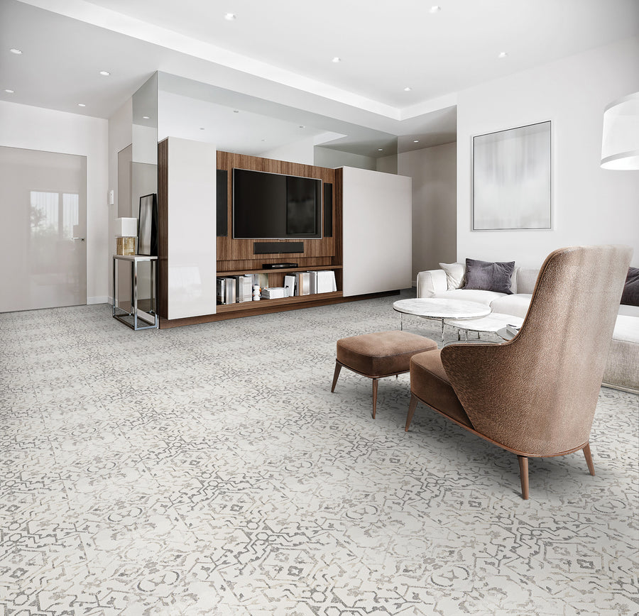 Modern living room with patterned light gray carpet, brown armchair and matching ottoman, round white coffee table, white sofa with cushions, wall-mounted TV, wood entertainment center, and neutral decor.