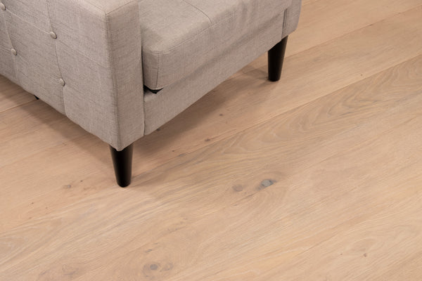 Corner of a light gray upholstered sofa with dark wooden legs on light-colored wooden flooring.