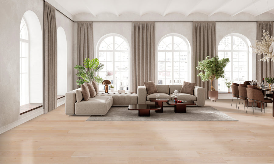 Spacious, modern living room with arched windows, beige sectional sofas, a gray rug, coffee tables, indoor plants, and a dining area with a long table and chairs; soft natural light fills the room.