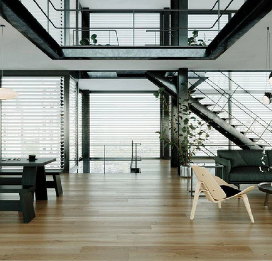 Modern, open-concept living space with large windows, Commercial Hardwood flooring, metal staircase, black dining table, green sofa, light wooden chair, and indoor plants. Natural light fills the room.