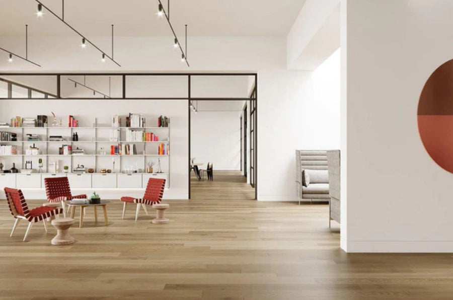 Modern office features Commercial Hardwood flooring, red lounge chairs, round tables, a wall bookshelf, glass meeting rooms in the back, plus a gray high-back sofa and circular wall art.