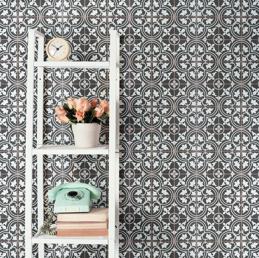 A white shelving unit with a clock, a potted bouquet of pink roses, a mint green rotary phone, and stacked books sits against a wall with a black and white ornate tile-patterned wallpaper.