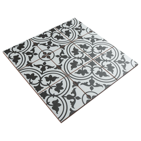 A square ceramic tile with a black and white vintage-style intricate floral and geometric pattern, divided into nine smaller squares with thin, brown grid lines.