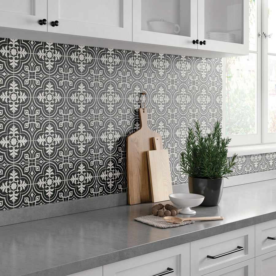 Modern kitchen with white cabinets, a gray countertop, and a black and white patterned tile backsplash. On the counter are wooden cutting boards, a potted plant, a bowl, and some cookies. Sunlight streams through the window.