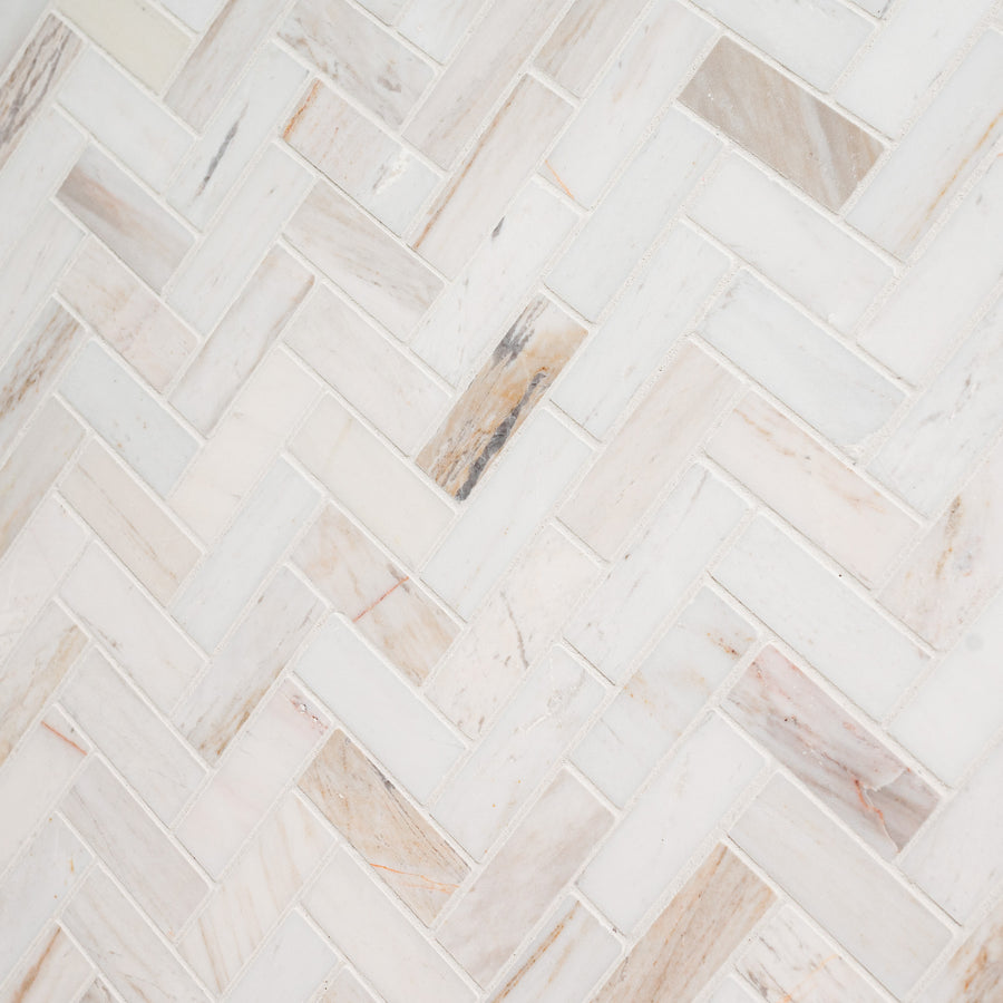 Close-up of Angora 12" x 12" Mosaic in Herringbone Polish, showing light-colored tiles with beige, gray, and cream veining arranged in a herringbone pattern for an elegant, textured look.