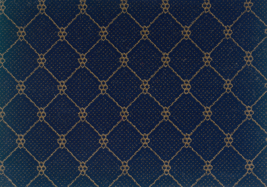 A close-up of Lake Boden Berber Carpet in Indigo showcases a dark blue textured surface with a repeating gold diamond crisscross pattern and small circular accents—ideal for stylish, durable modern home flooring.