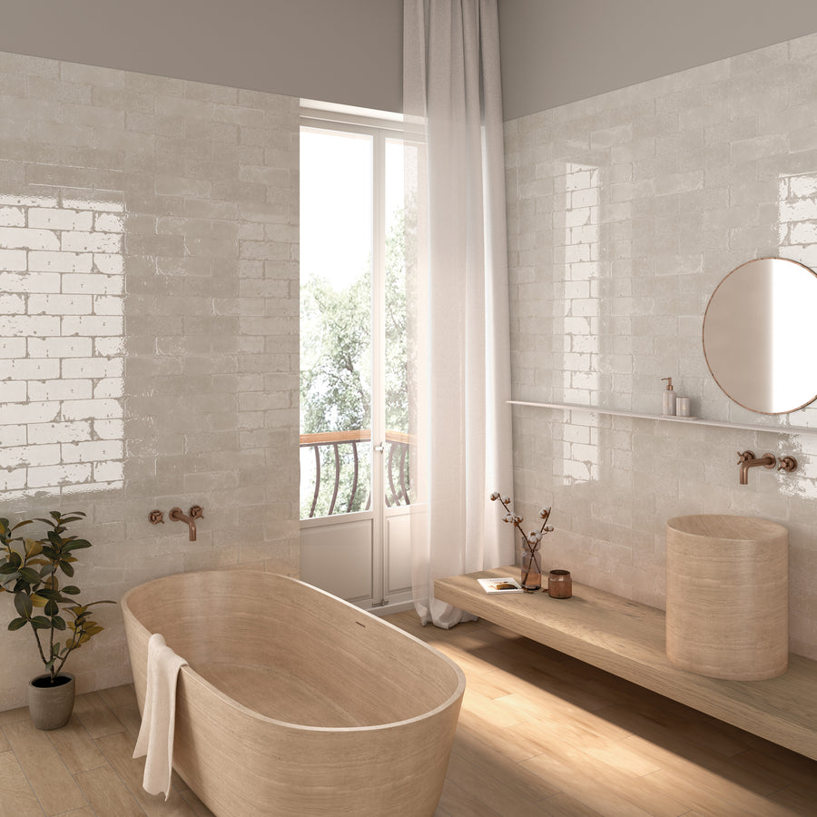 A modern, minimalist bathroom with light wood fixtures, a freestanding tub, a round sink, a circular mirror, a potted plant, and a large window with white curtains letting in natural light.