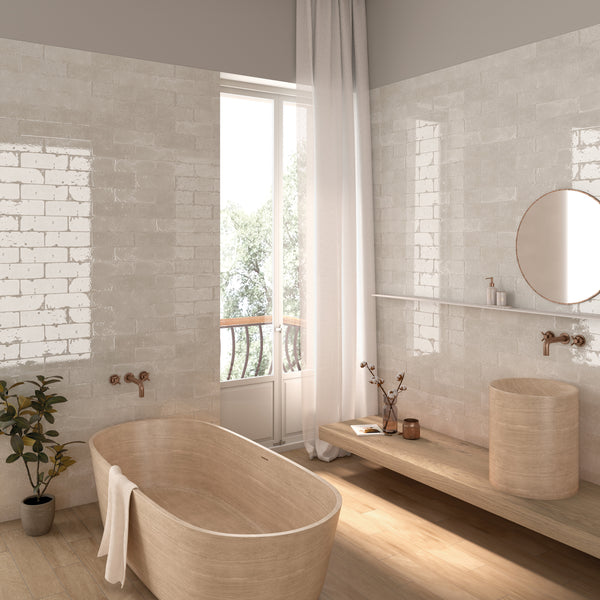 A modern, minimalist bathroom with light wood fixtures, a freestanding tub, a round sink, a circular mirror, a potted plant, and a large window with white curtains letting in natural light.