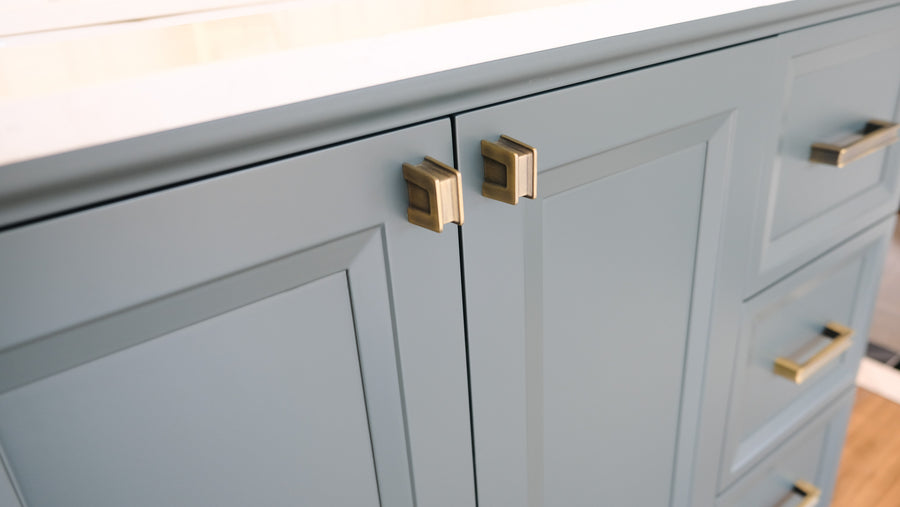Close-up of blue cabinet doors and drawers with modern rectangular gold handles, topped with a white countertop.