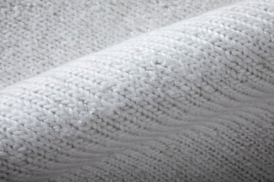 Close-up of a soft, white, knitted fabric with visible textured stitches and a slight diagonal fold.