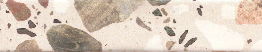 A close-up of Fragmento 2x10 Ceramic Tile in Just Peachy, featuring a terrazzo look with bold patterns of large and small brown, gray, and beige stone fragments set in a light peach background.