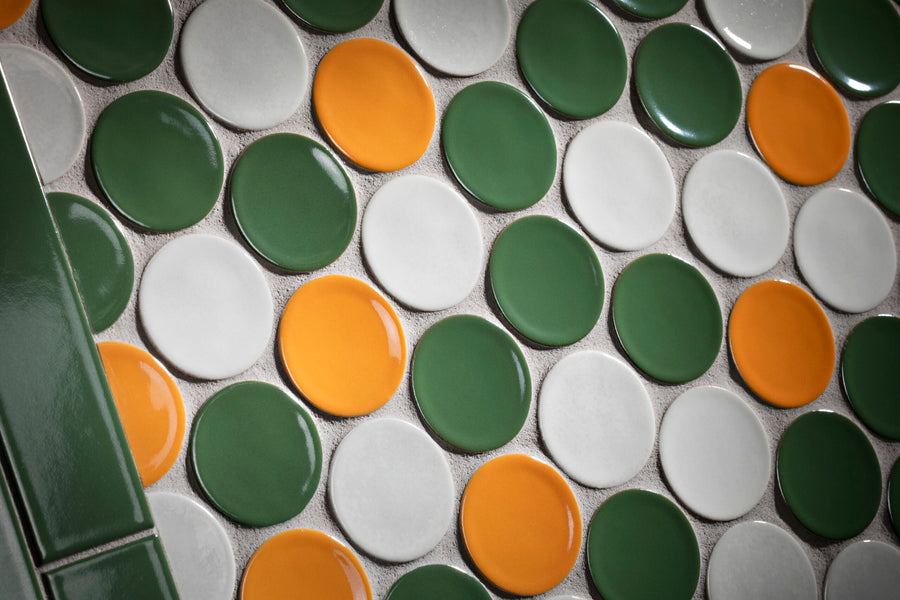 Close-up of round ceramic tiles in green, orange, and white arranged in a repeating pattern; vertical rectangular green tiles are visible on the left side of the image.