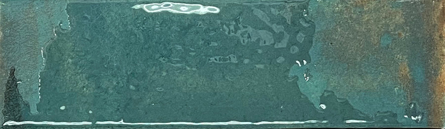 A rectangular Kinetic 2.5x9 Porcelain Subway Tile in the Shifting Skies color, featuring a mottled teal surface with textured variations and patches of brownish rust along the right edge, reminiscent of artisanal pottery finishes.