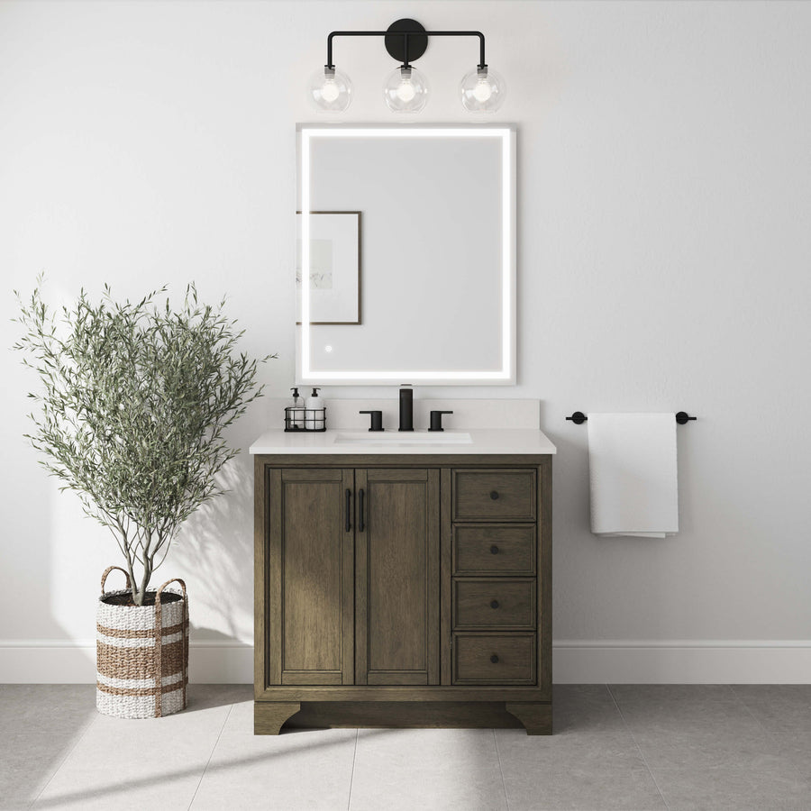 A modern bathroom with a wooden vanity, black fixtures, a square backlit mirror, a three-bulb light fixture, a towel on the wall, a basket with towels, and a potted olive tree on a light gray floor.