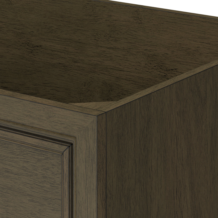 Close-up of the corner of a dark wood cabinet with a raised panel door, showing the grain and texture of the wood and the detailed edges of the frame.