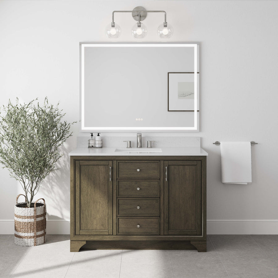 A modern bathroom includes the Lanagan 48" Vanity with a white countertop, a rectangular LED-lit mirror, a three-light fixture above, a wall-mounted towel, framed art on the wall, and a potted plant in a wicker basket.