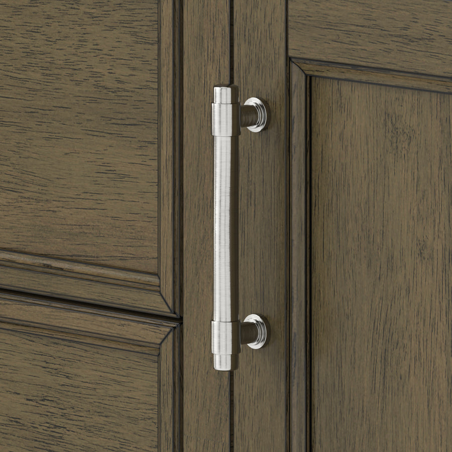 Silver metal cabinet handle with cylindrical shape mounted vertically on a wooden cabinet door with a brown, textured finish and panel detailing.