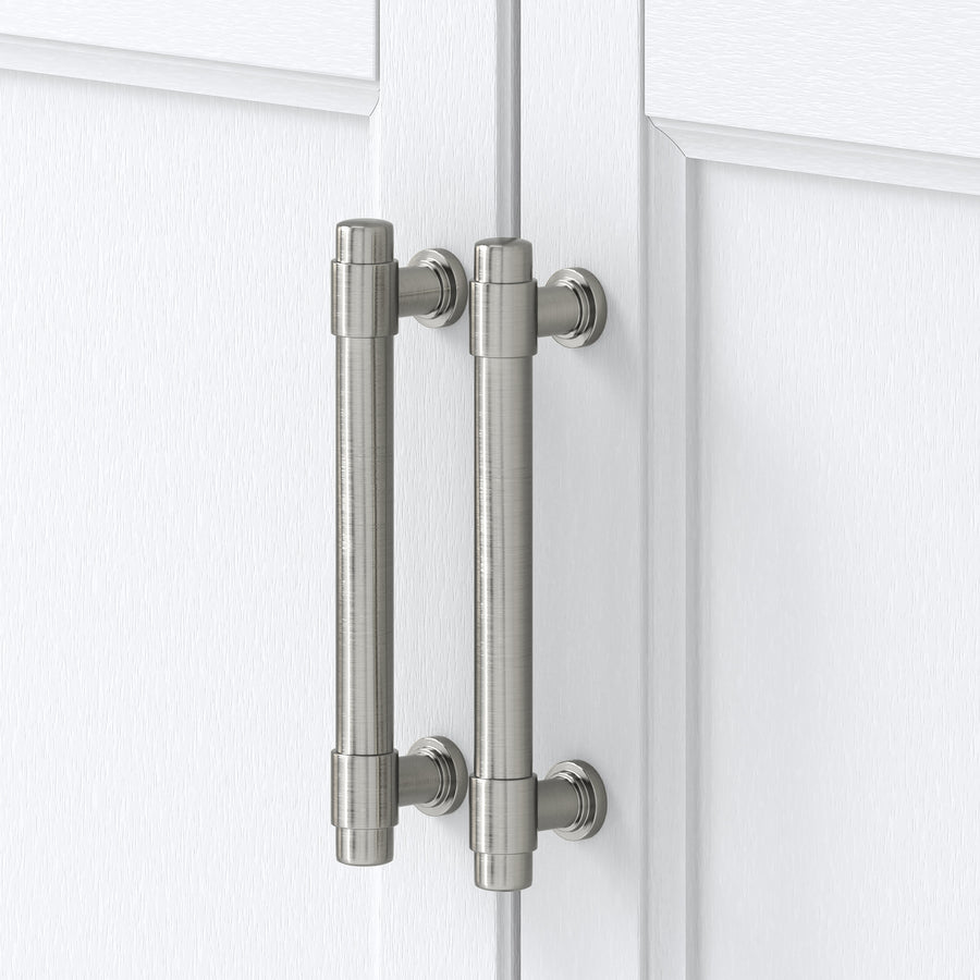 Close-up of two brushed nickel cabinet handles mounted vertically on white cabinet doors. The handles are cylindrical with decorative end caps and are placed side by side where the doors meet.
