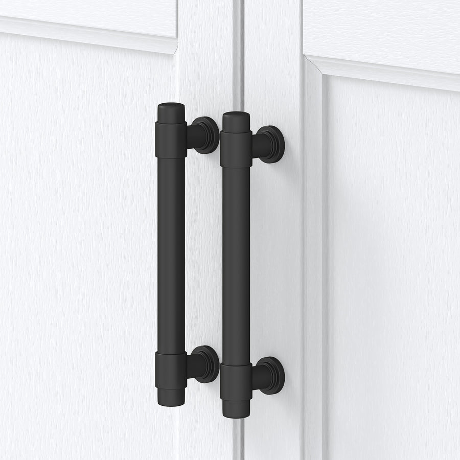 Two matte black cylindrical cabinet handles are mounted vertically on adjacent white cabinet doors with a slight gap between the handles. The handles have round bases and a modern, industrial design.