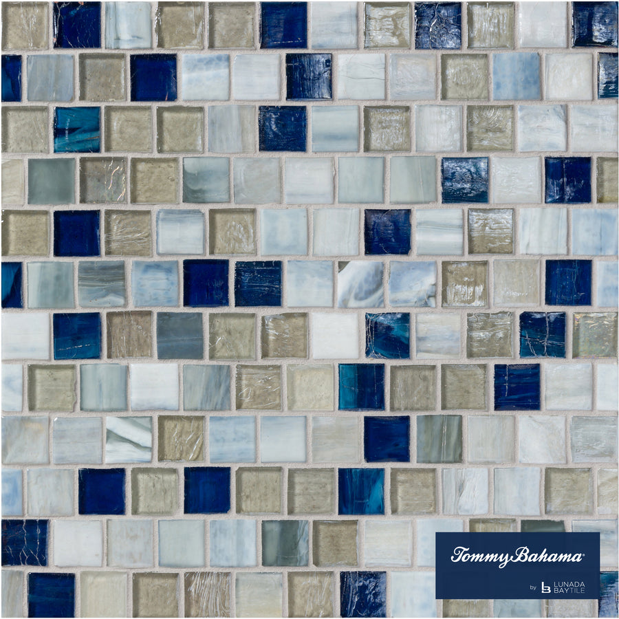 A mosaic tile wall featuring the Tommy Bahama Offset Mosaic Tile in Motuo Mix, showcasing blue, gray, white, and tan hues—some with a marbled finish. Ideal for accent walls, with the Tommy Bahama logo in the bottom right corner.