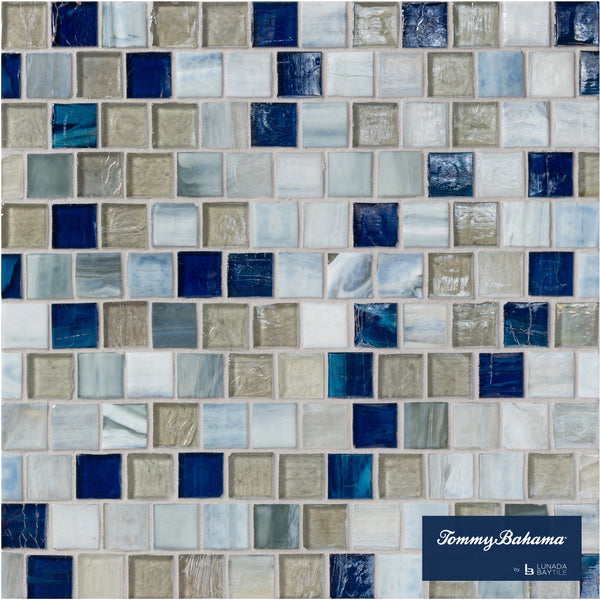 A mosaic tile wall featuring the Tommy Bahama Offset Mosaic Tile in Motuo Mix, showcasing blue, gray, white, and tan hues—some with a marbled finish. Ideal for accent walls, with the Tommy Bahama logo in the bottom right corner.