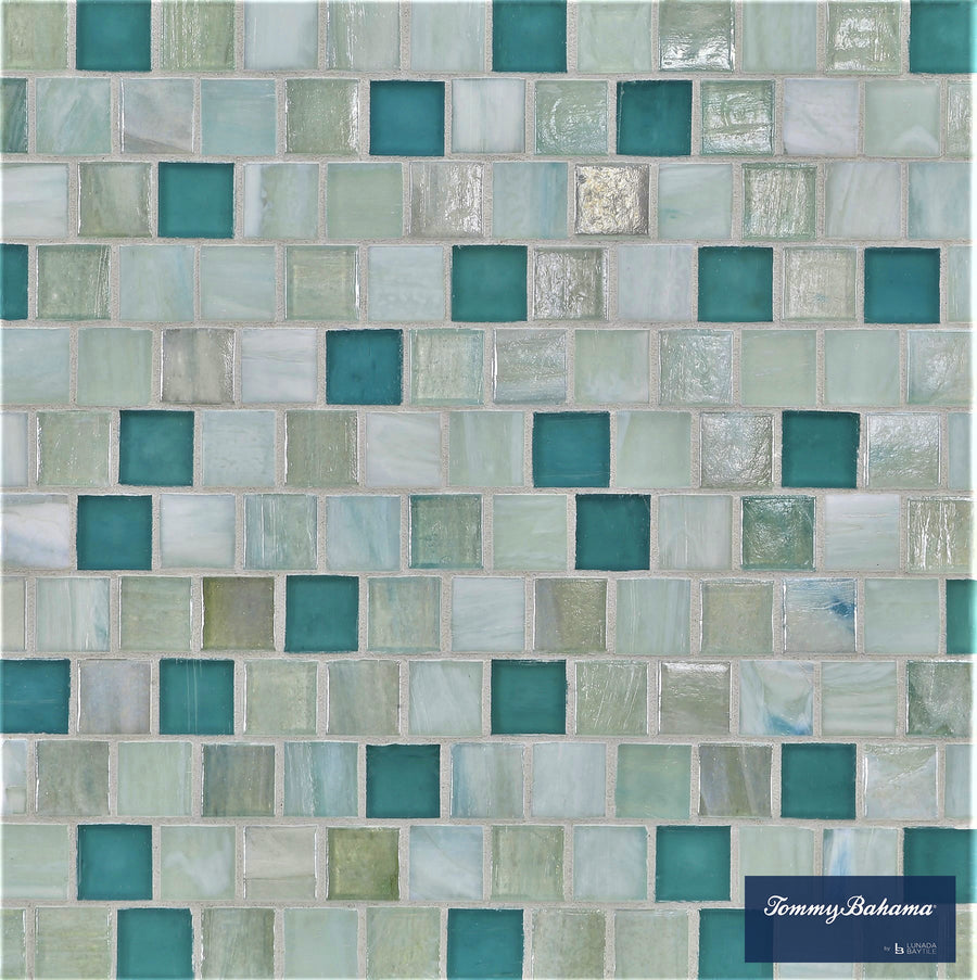 The Tommy Bahama Offset Mosaic Tile in San Blas Mix features small square tiles in tranquil shades, creating a serene accent wall. The blue label with the logo appears in the bottom right corner of the packaging.