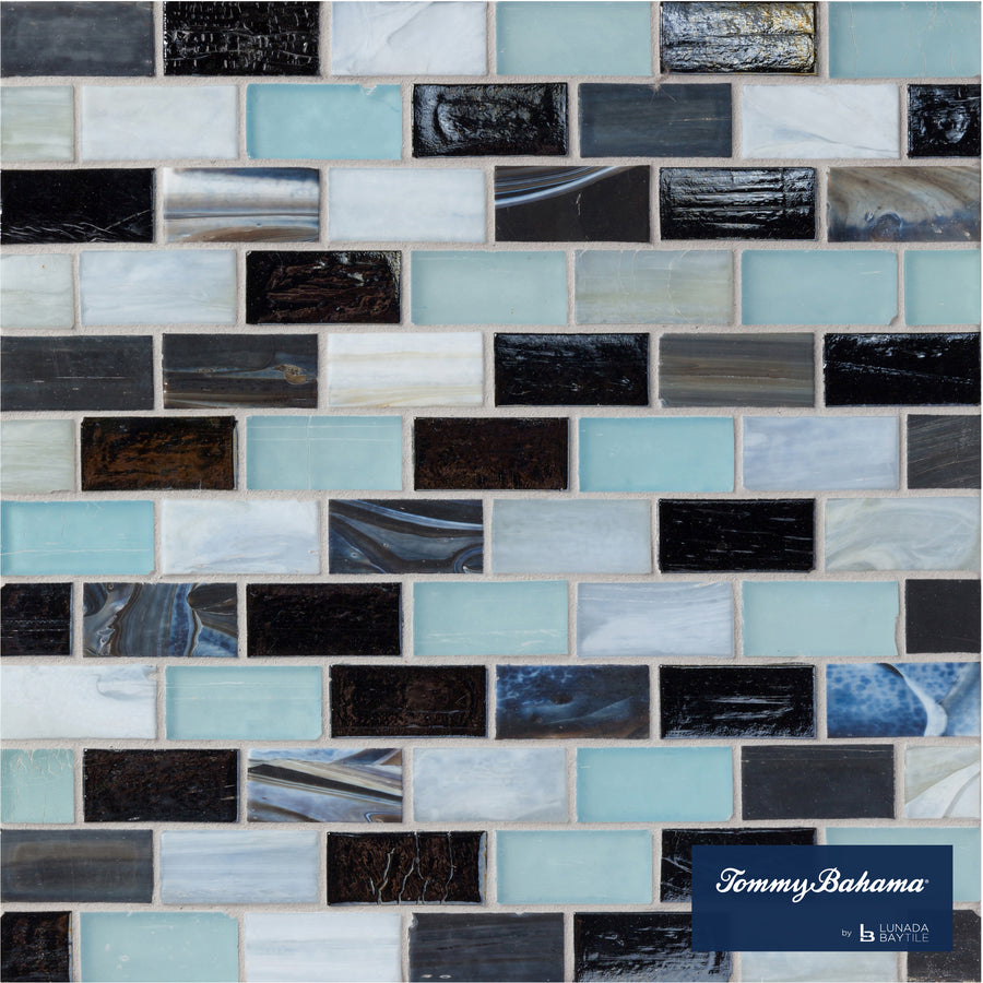 The Tommy Bahama 1 sf/sh Brick Ceramic Tile in Fujisan Mix features a mosaic of rectangular tiles in black, white, light blue, and gray with varied textures. The Tommy Bahama logo is displayed in the bottom right corner.