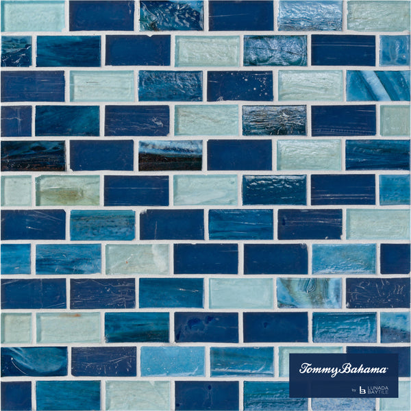 A close-up of a wall with Tommy Bahama 1 sf/sh Brick Ceramic Tile in Lucky Bay Mix, showing rectangular tiles in varying blue and aqua shades. The bottom right has the 