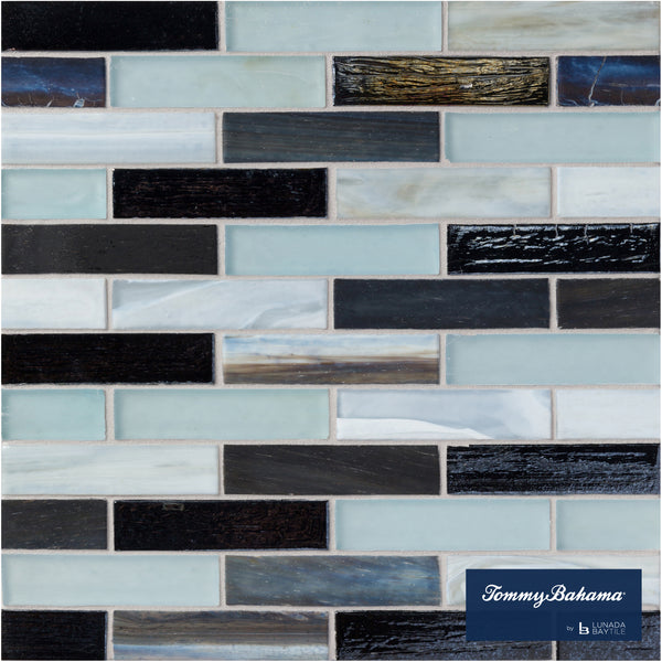 The Tommy Bahama 0.85 sf/sh Brick Ceramic Tile in Fujisan Mix features rectangular glass mosaic tiles in black, gray, white, and light blue arranged in a brick pattern, with a Tommy Bahama logo in the bottom right corner.