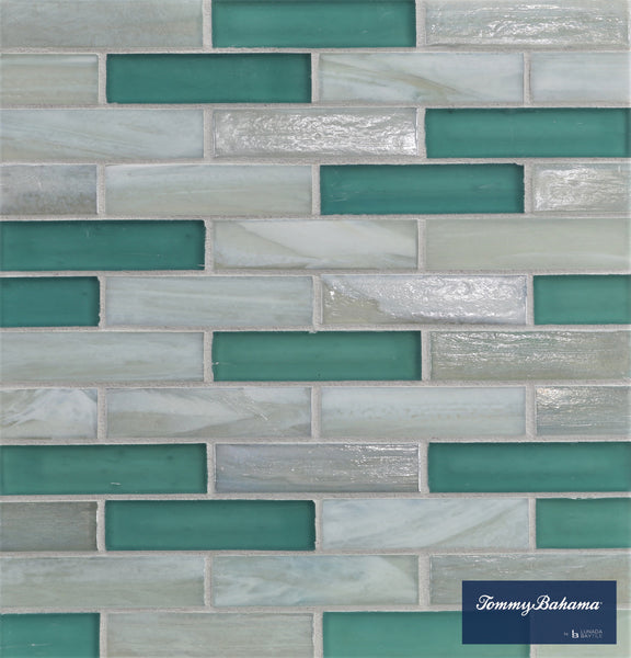 A wall of Tommy Bahama 0.85 sf/sh Brick Ceramic Tile in San Blas Mix—rectangular tiles with aqua, teal, and light gray tones arranged in a brick pattern. A blue label at the bottom right reads Tommy Bahama.