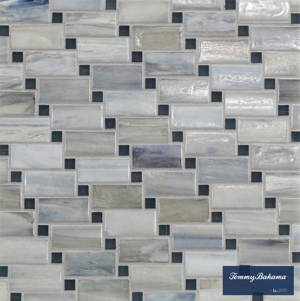 The Tommy Bahama Vineyard Mosaic Tile in Twillingate Mix features rectangular ceramic tiles in gray, blue, and white, arranged in an offset brick pattern—ideal for accent walls. The lower right corner shows the Tommy Bahama logo.